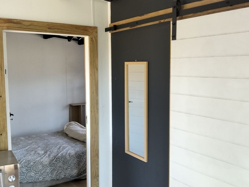 A bedroom interior featuring a modern sliding barn door, exposed ceiling beams, and contrasting timber and dark wall paneling.