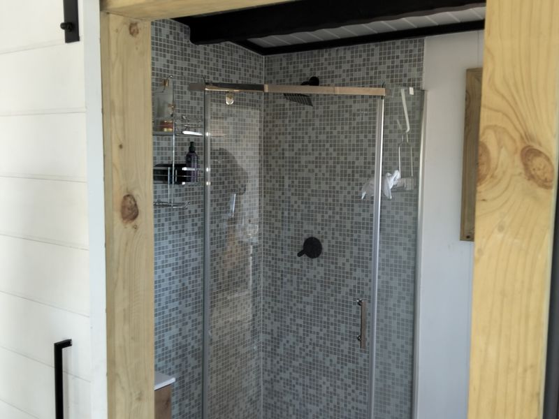 A modern bathroom featuring a glass-enclosed shower with mosaic tiling and a rustic timber-framed sliding barn door entrance.