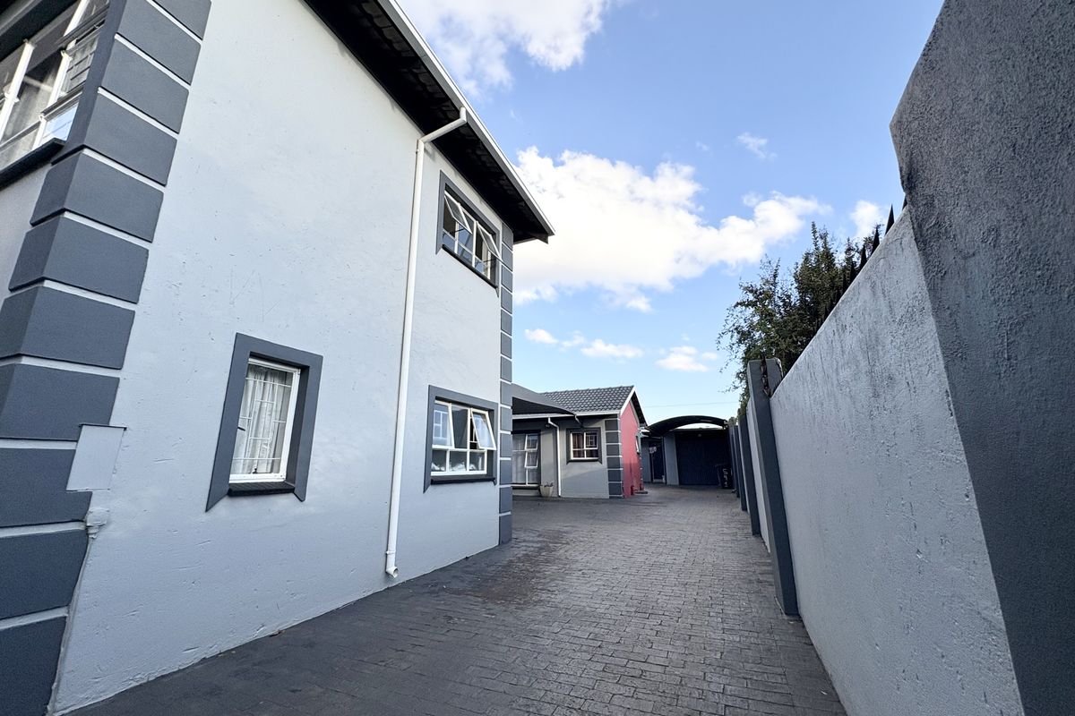 A view of the paved side driveway and rear exterior of the property, featuring boundary walls and established building facades.