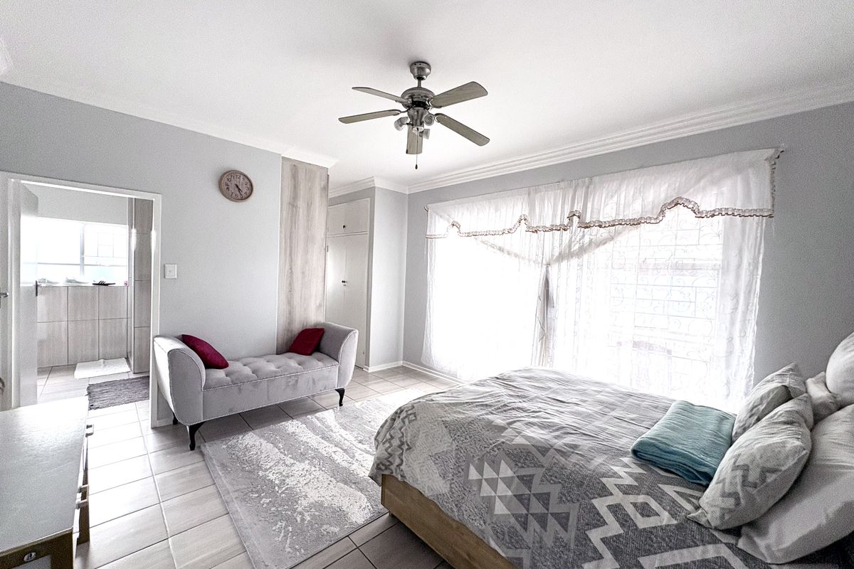 A well-maintained bedroom featuring tiled flooring, a ceiling fan, and built-in cupboards, with an adjoining en-suite bathroom visible.