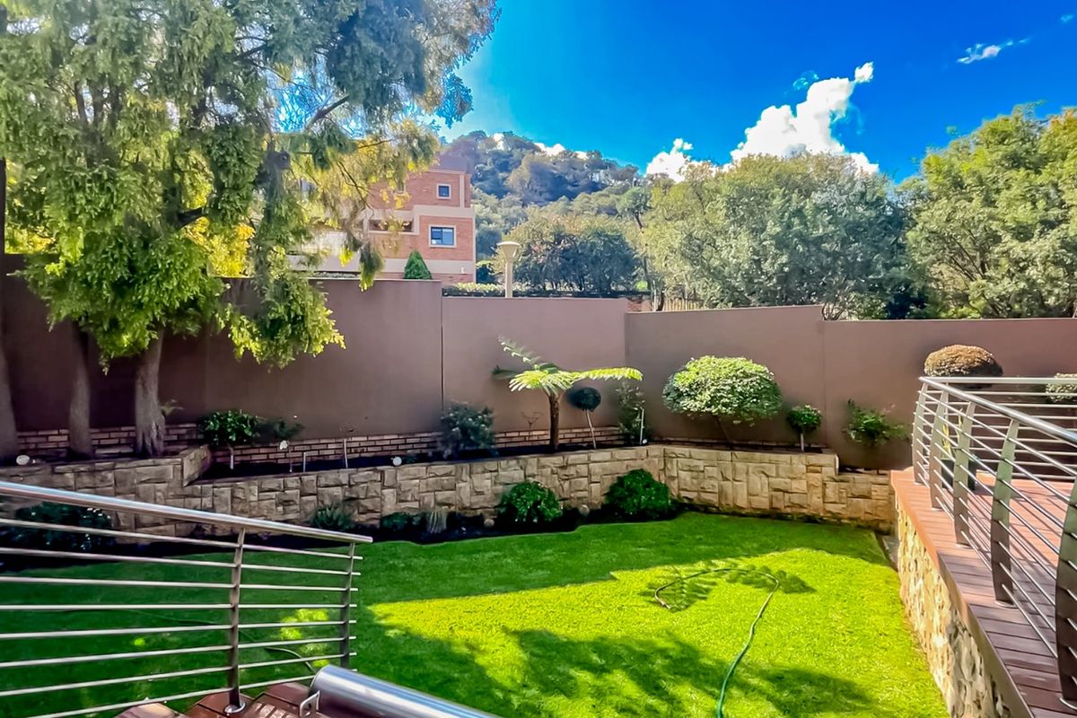 A well-maintained rear garden featuring a manicured lawn, stone-clad retaining walls, and a raised timber deck with stainless steel railings.