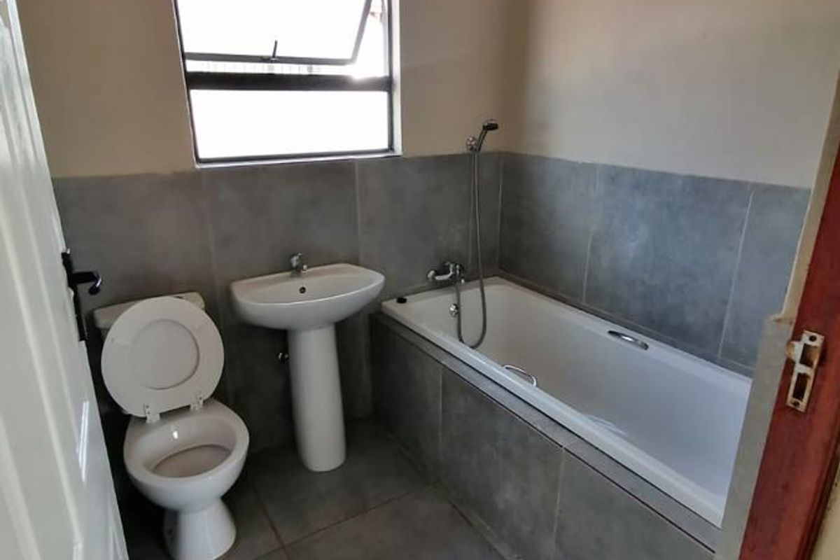 A clean, modern bathroom featuring a pedestal basin, toilet, and a bathtub with a handheld shower mixer, finished with neutral grey wall and floor tiles.