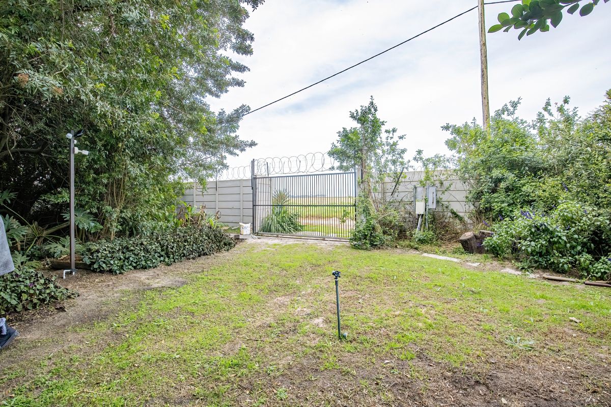 A rear garden area featuring a secure metal gate with razor wire, precast concrete boundary walls, and an irrigation sprinkler system.