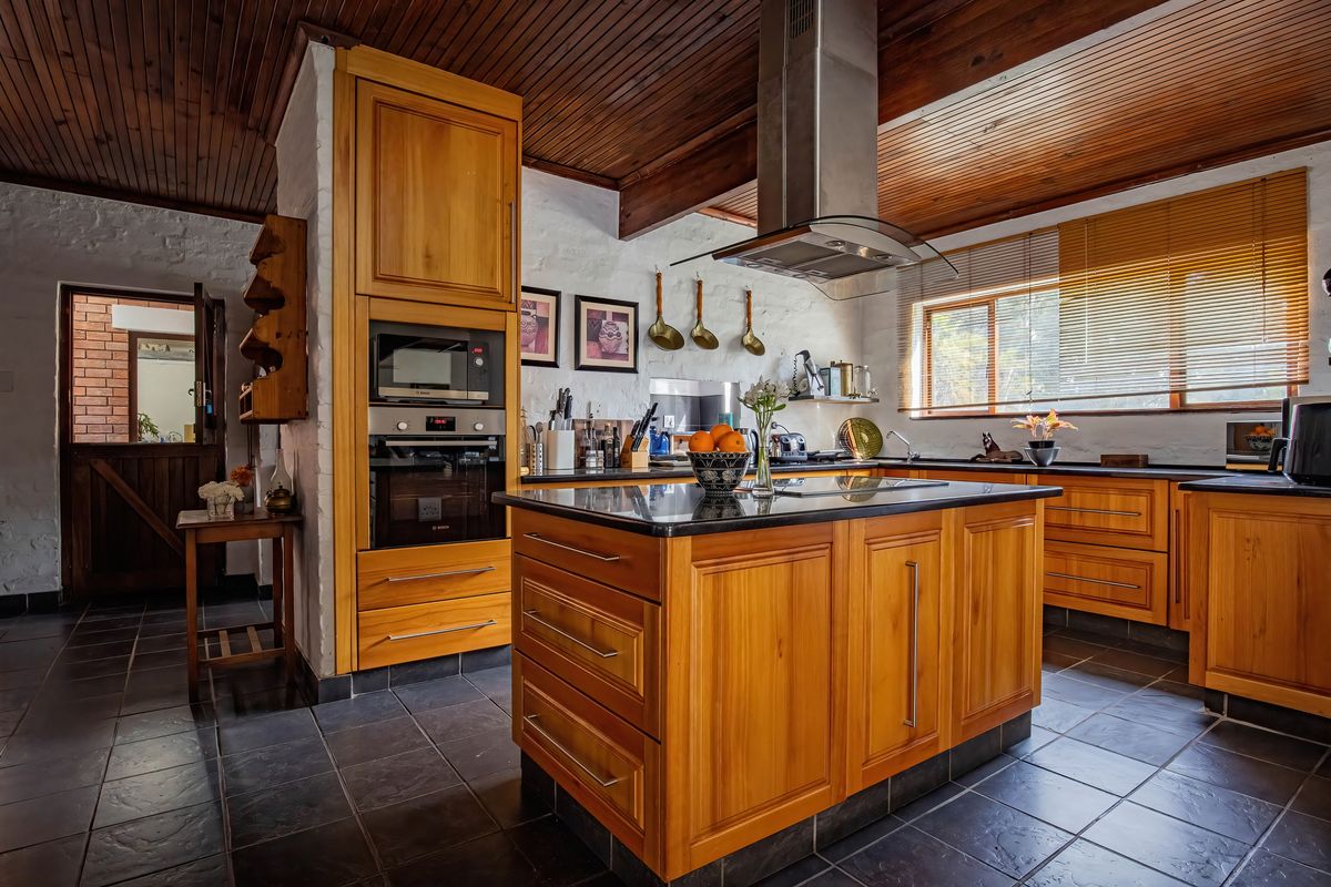 A well-maintained kitchen featuring warm wooden cabinetry, a central island with granite countertops, built-in appliances, and a distinctive timber-clad ceiling.