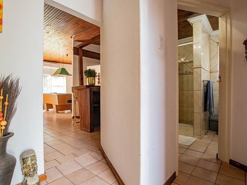 A central hallway providing access to a living area with a built-in bar and a tiled bathroom with a shower.