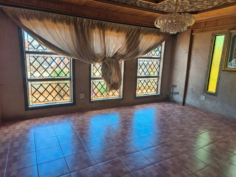 Spacious living area featuring tiled flooring, a timber-paneled ceiling, a crystal chandelier, and large windows with security burglar bars.