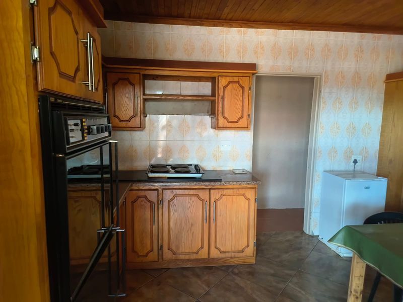A functional kitchen featuring traditional wooden cabinetry, a built-in oven, electric hob, and tiled finishes, offering potential for a modern cosmetic update.