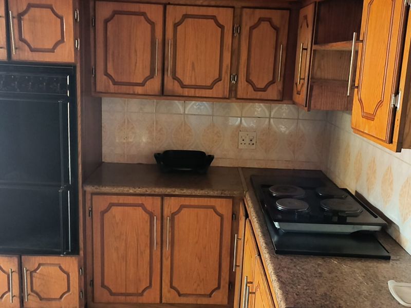 A dated kitchen featuring wood-tone cabinetry, a built-in oven, electric hob, and tiled backsplash, offering potential for a modern renovation.