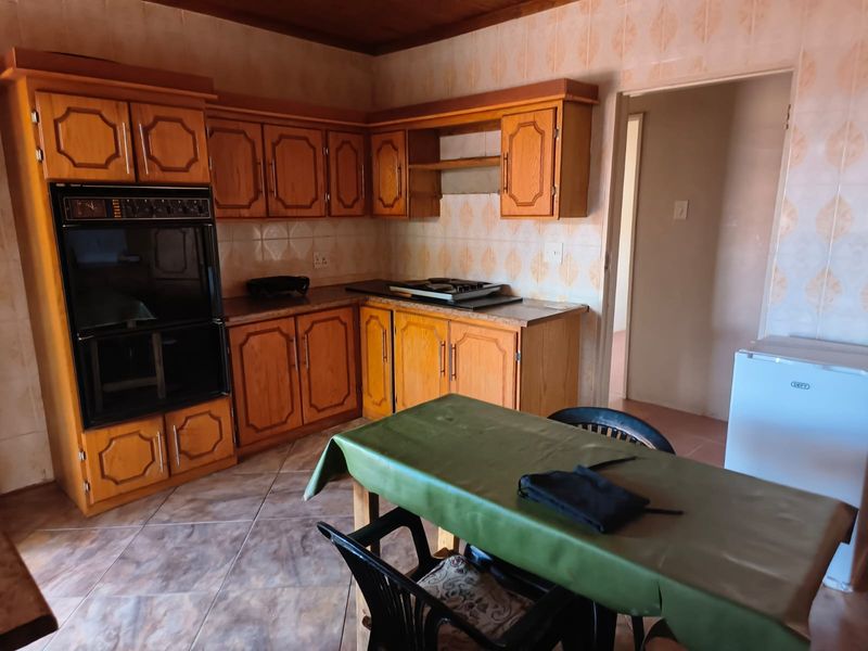 A dated kitchen featuring traditional wooden cabinetry, built-in oven and hob, tiled splashbacks, and tiled flooring with a timber ceiling.