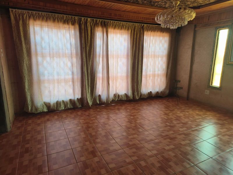Spacious living area featuring timber ceiling paneling, ceramic floor tiles, and a classic crystal chandelier, offering a blank canvas for modern interior design.