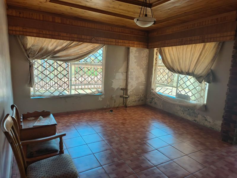 Living room featuring timber ceiling and tiled flooring, currently showing significant wall surface deterioration and peeling paint requiring maintenance.