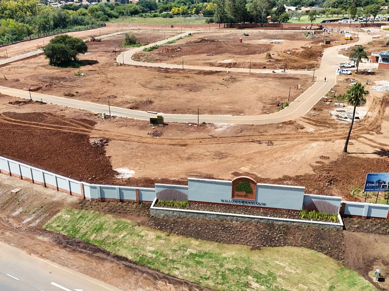 Aerial view of a residential development site featuring cleared land, paved internal roads, perimeter walling, and entrance signage.