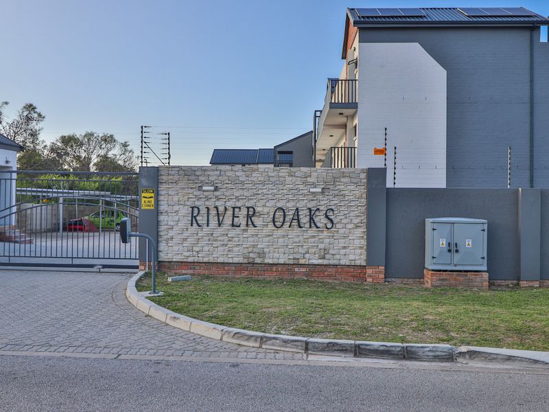 The entrance to River Oaks apartment complex featuring a stone-clad signage wall, secure metal gate, and perimeter electric fencing.