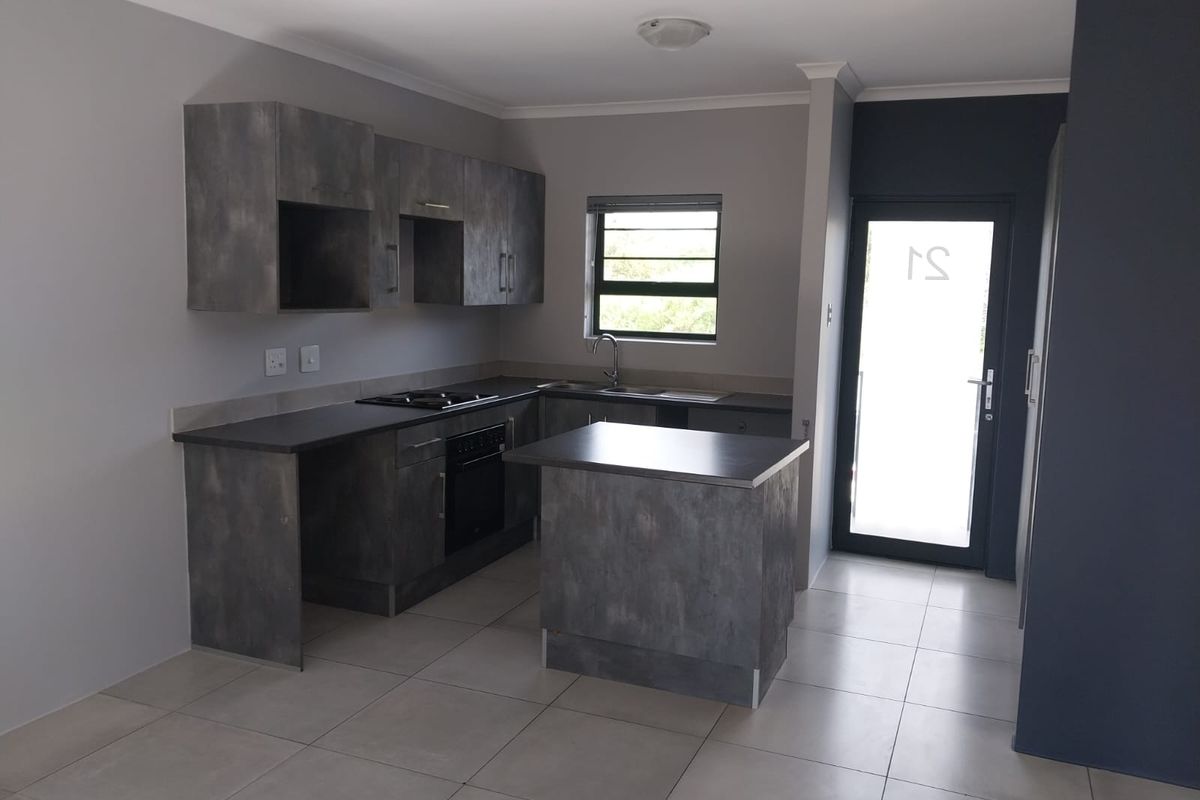 A modern, empty kitchen featuring dark grey cabinetry, built-in oven and hob, tiled flooring, and direct access to an exterior door.