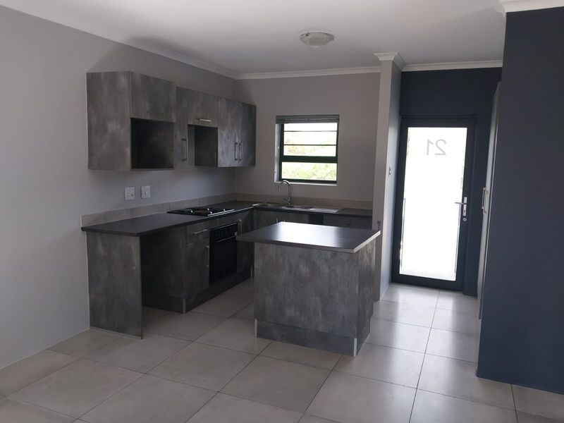 A modern, empty kitchen featuring dark grey cabinetry, built-in oven and hob, tiled flooring, and direct access to an exterior door.