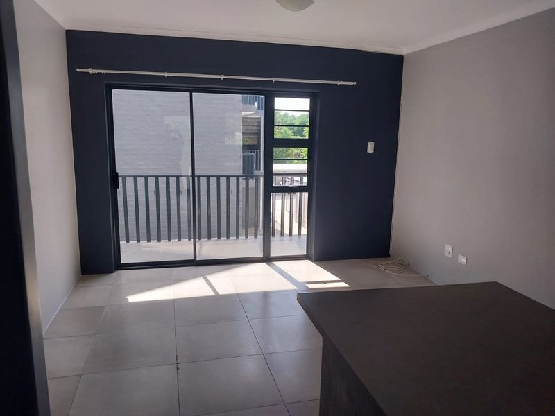 An open-plan living area featuring neutral tiled flooring, a dark accent wall, and a large sliding glass door leading to a balcony.