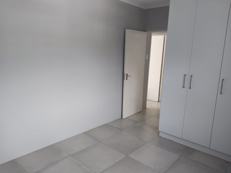 A clean, empty bedroom featuring neutral grey tiled flooring and modern built-in cupboards, offering a blank canvas for personalization.