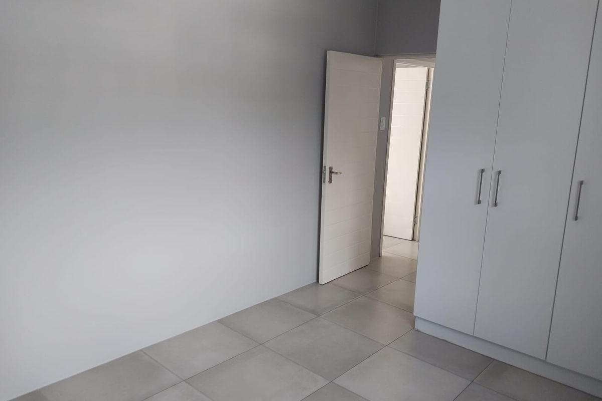 A clean, empty bedroom featuring neutral grey tiled flooring and modern built-in cupboards, offering a blank canvas for personalization.