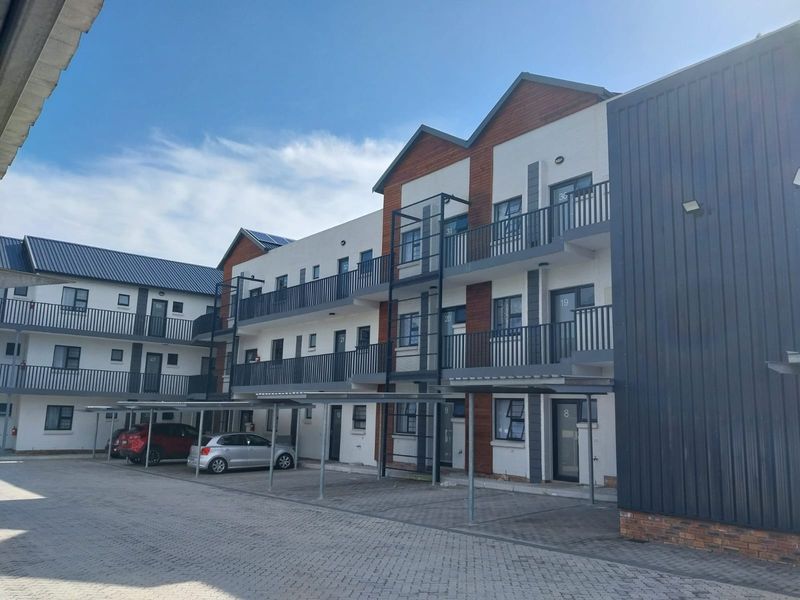 Exterior view of a modern multi-story apartment complex featuring paved parking, covered carports, and private balconies with metal railings.