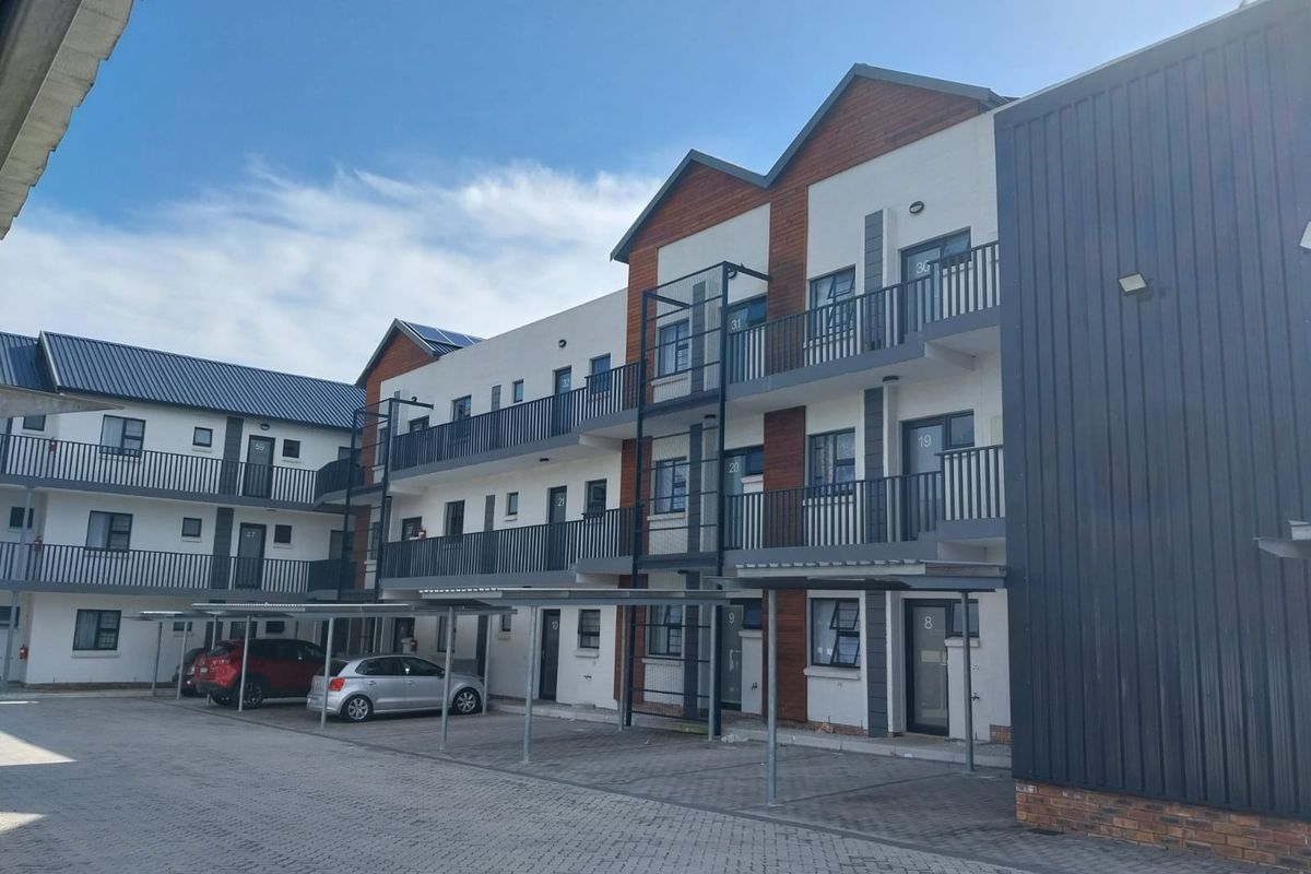 Exterior view of a modern multi-story apartment complex featuring paved parking, covered carports, and private balconies with metal railings.