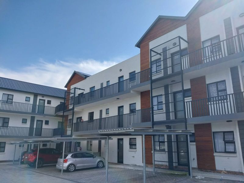 A multi-story apartment complex featuring modern timber cladding, metal balustrades, and covered parking bays on a paved driveway.