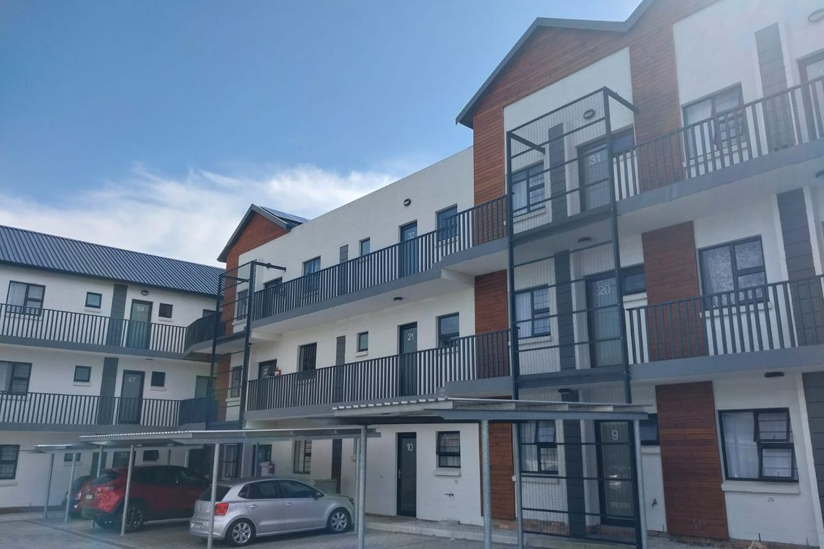 A multi-story apartment complex featuring modern timber cladding, metal balustrades, and covered parking bays on a paved driveway.