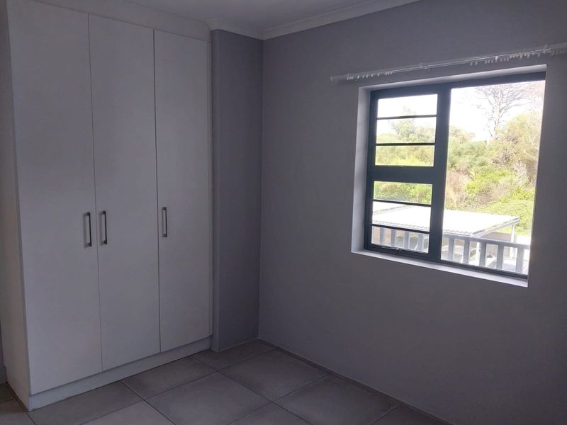 A clean, empty bedroom featuring neutral grey walls, tiled flooring, and built-in cupboards with a window overlooking the exterior.