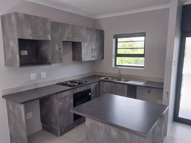 Modern kitchen featuring grey textured cabinetry, dark laminate countertops, built-in oven and hob, and a functional double sink setup.