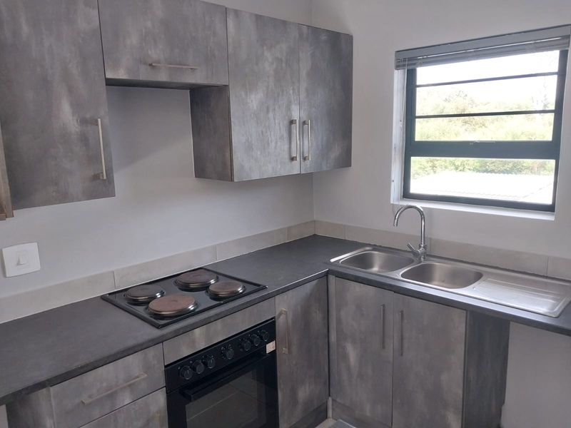 Modern kitchen featuring grey textured cabinetry, dark laminate countertops, a built-in electric oven and hob, and a double sink with a mixer tap.