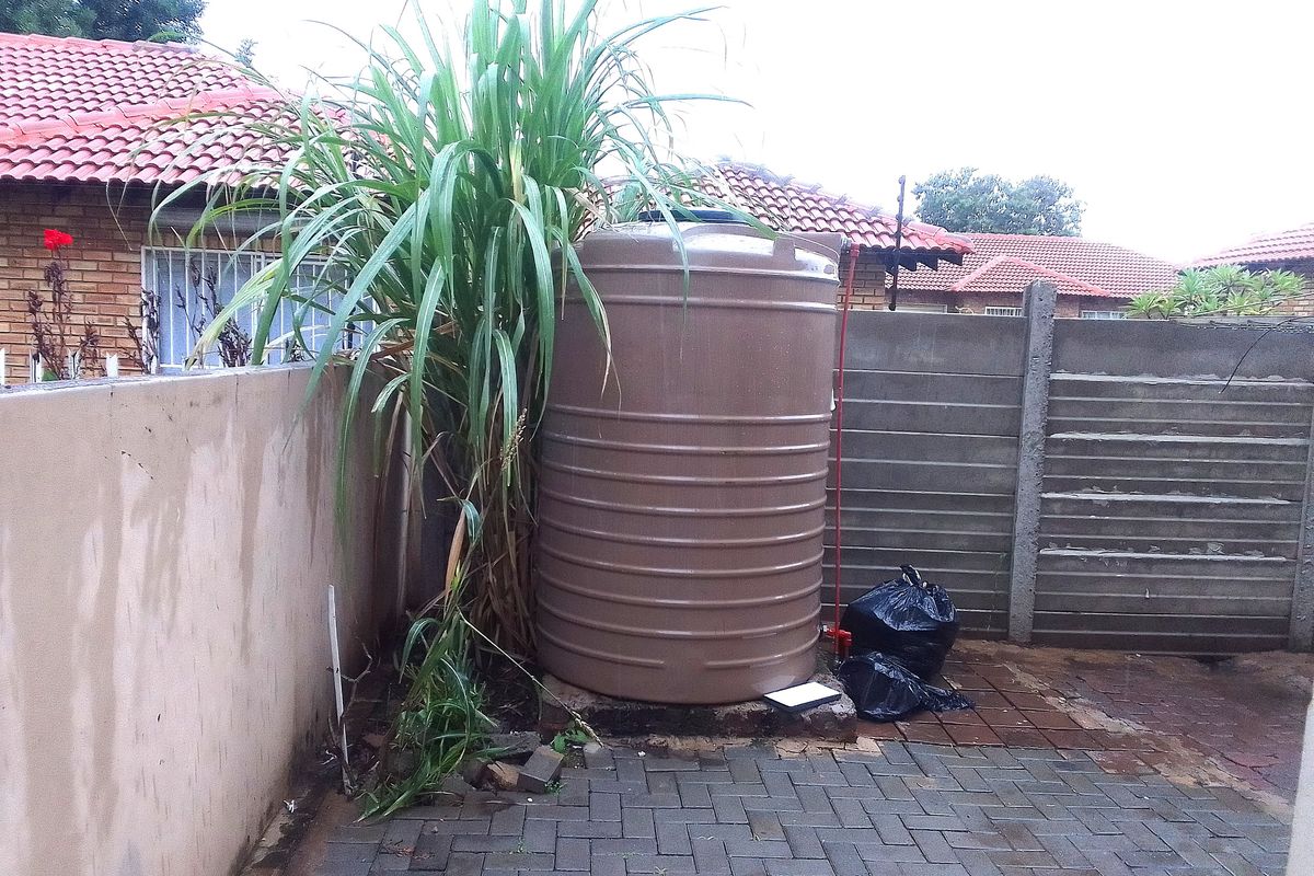 Rear exterior area featuring a water storage tank, paved patio surface, and precast concrete boundary walling.