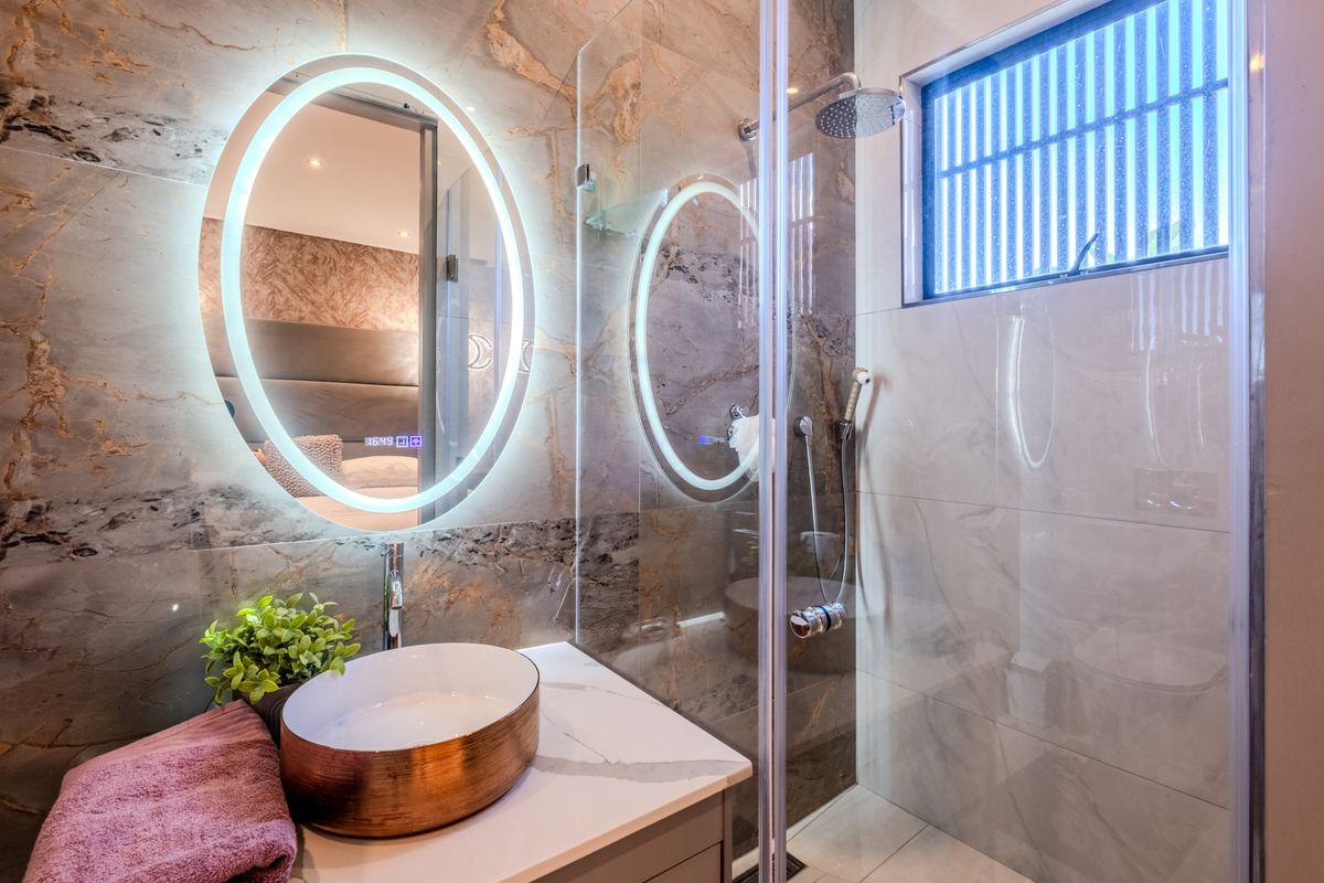 Modern bathroom featuring a vessel sink on a stone vanity, LED backlit mirror, and a glass-enclosed shower with premium tiled finishes.