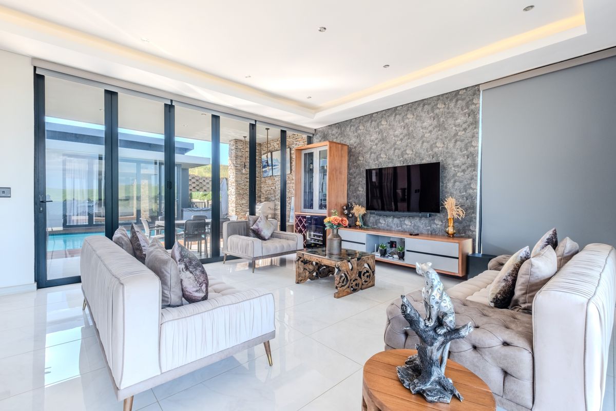 Modern living room featuring large format floor tiles, recessed cove lighting, and expansive floor-to-ceiling glass sliding doors providing seamless access to the outdoor pool area.