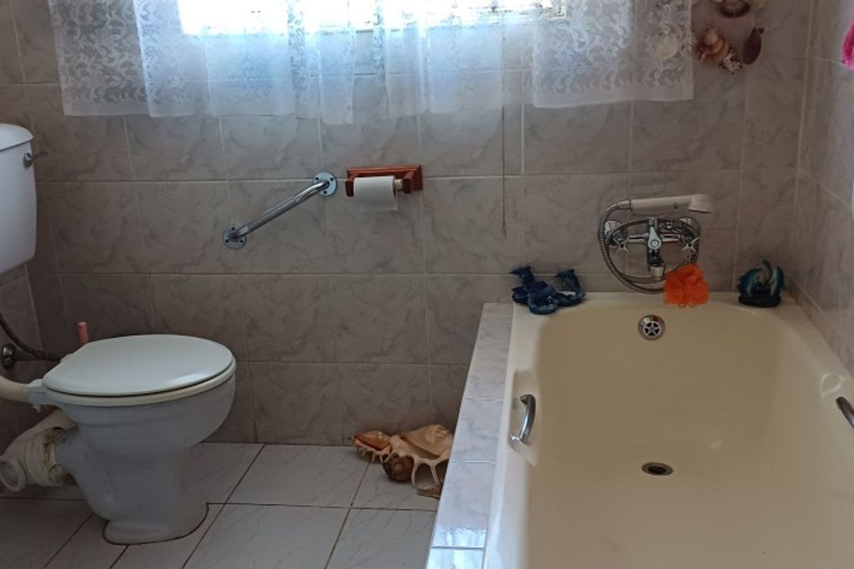 A functional bathroom featuring a bathtub, toilet, and vanity basin with tiled walls and flooring, including a wall-mounted grab rail for accessibility.