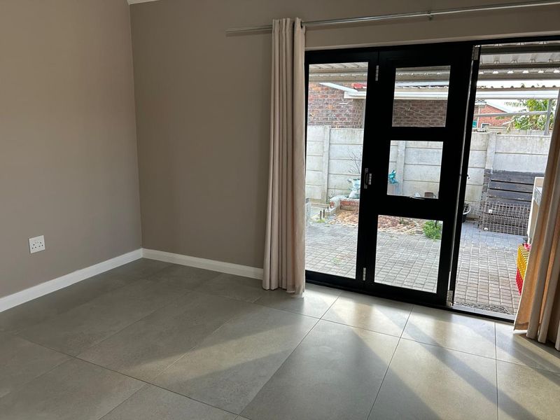 An empty living room featuring modern grey floor tiles and a black aluminium framed glass door providing access to the rear patio area.