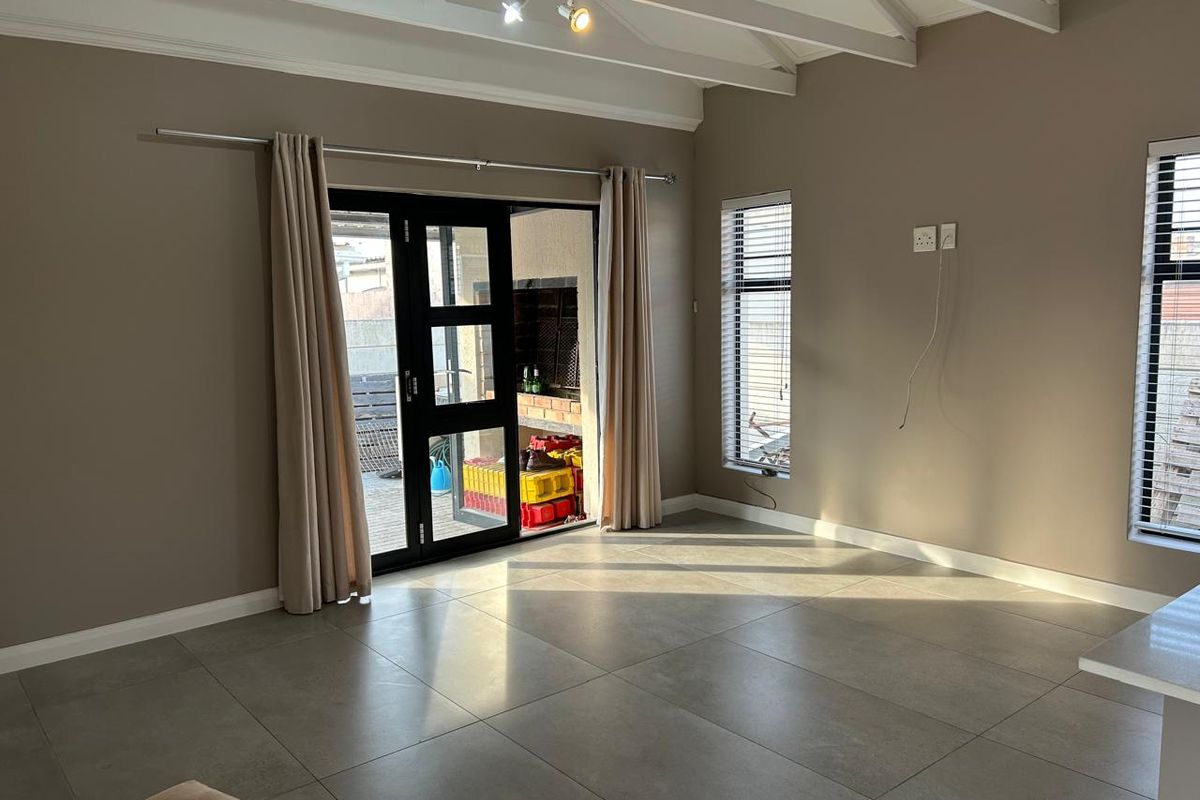 Spacious living area featuring large format floor tiles, exposed beam ceilings, and direct access to an outdoor patio with a built-in braai.