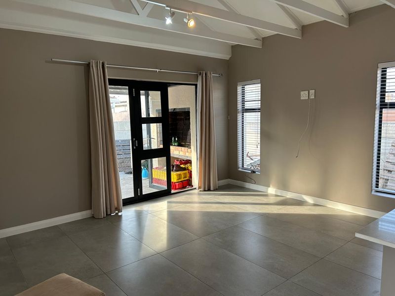 Spacious living area featuring large format floor tiles, exposed beam ceilings, and direct access to an outdoor patio with a built-in braai.