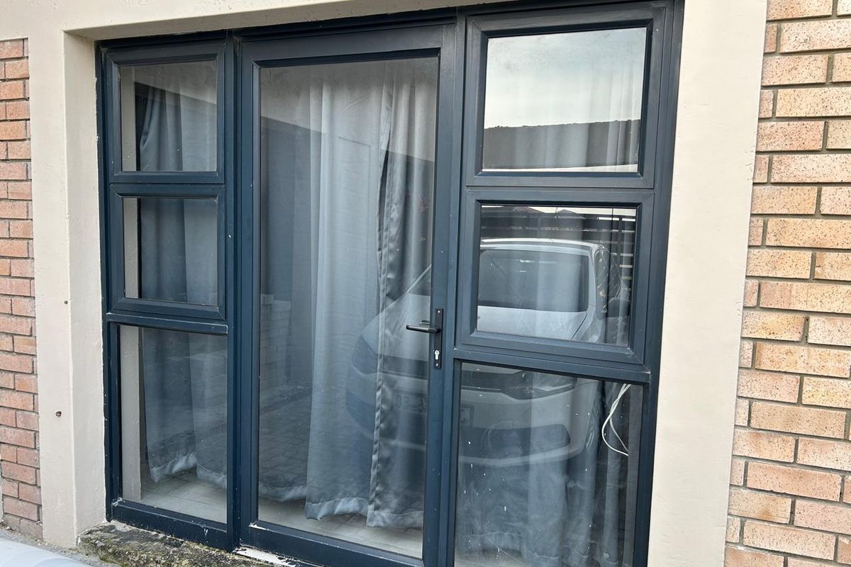 Exterior view of a dark grey aluminium framed glass door set within a brick facade, featuring a concrete threshold.