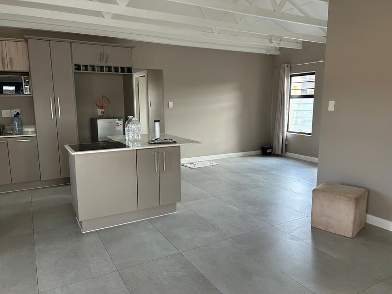 Modern open-plan living area featuring a sleek kitchen with built-in cabinetry, a central island with a cooktop, and large format floor tiles.
