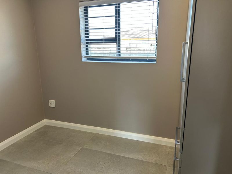 A clean, empty bedroom featuring neutral wall paint, large format floor tiles, and an aluminium window with fitted venetian blinds.