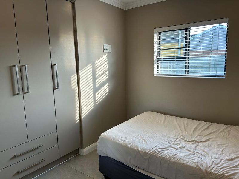 A well-maintained bedroom featuring neutral wall tones, built-in cabinetry, tiled flooring, and a window fitted with venetian blinds.