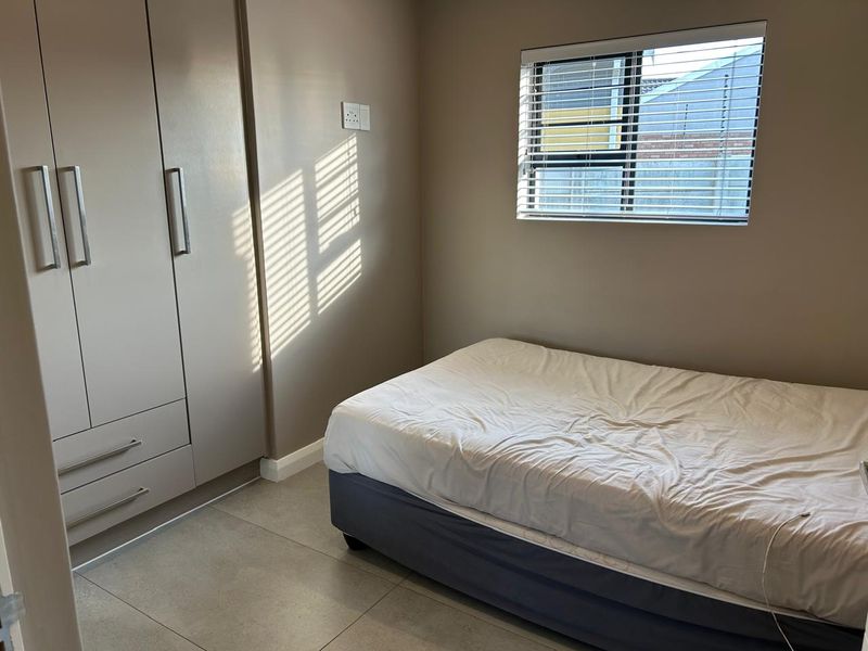A neat bedroom featuring built-in cupboards, tiled flooring, and a window fitted with venetian blinds, offering a clean and functional living space.