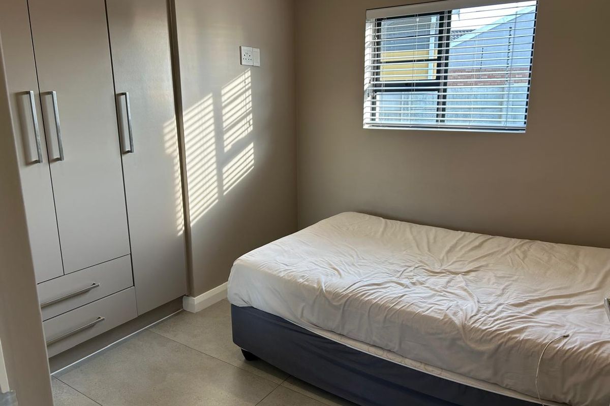 A neat bedroom featuring built-in cupboards, tiled flooring, and a window fitted with venetian blinds, offering a clean and functional living space.