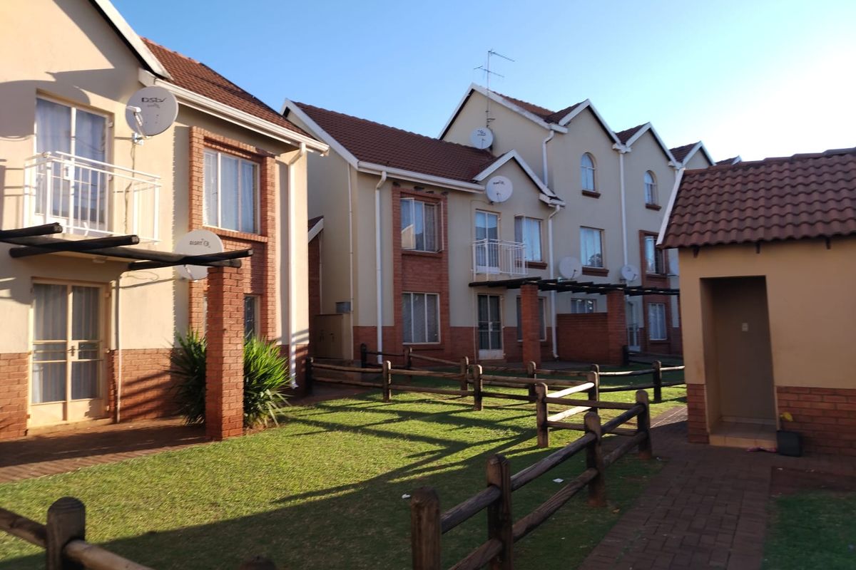Exterior view of a residential apartment complex featuring brick and plaster facades, tiled roofs, small balconies, and a shared garden area with paved walkways.