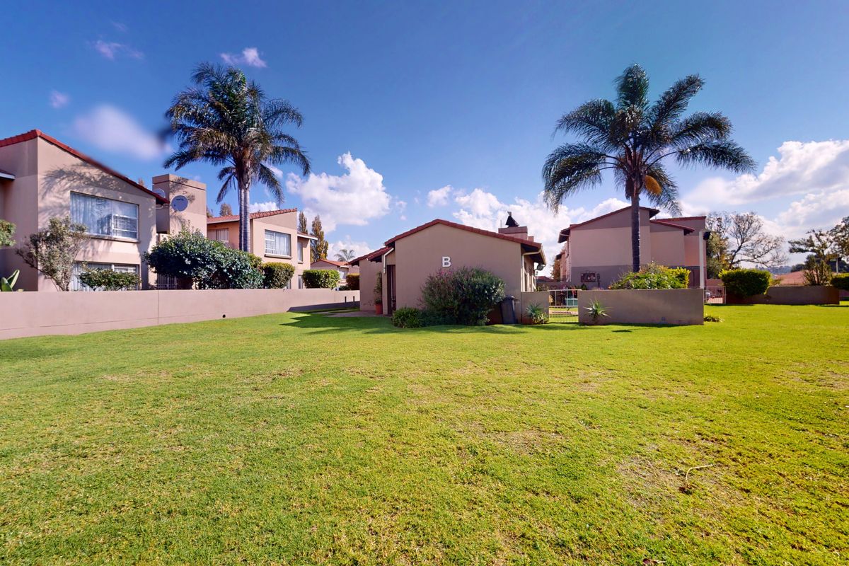 A view of the rear exterior of the apartment complex, featuring a well-maintained communal lawn, perimeter walls, and established palm trees.
