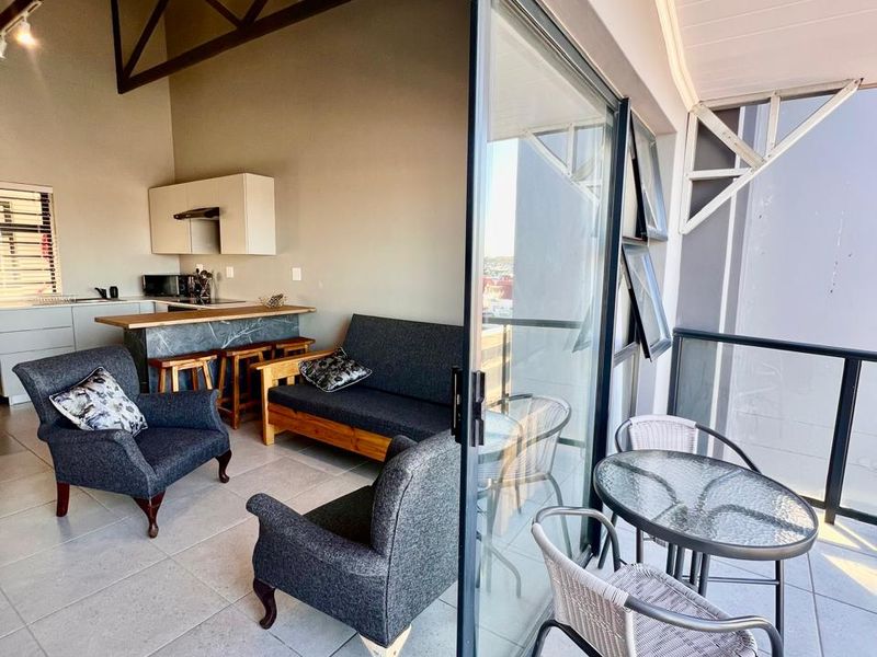 Open-plan living area featuring exposed roof trusses, a kitchen island, and seamless transition to a private balcony through large sliding glass doors.