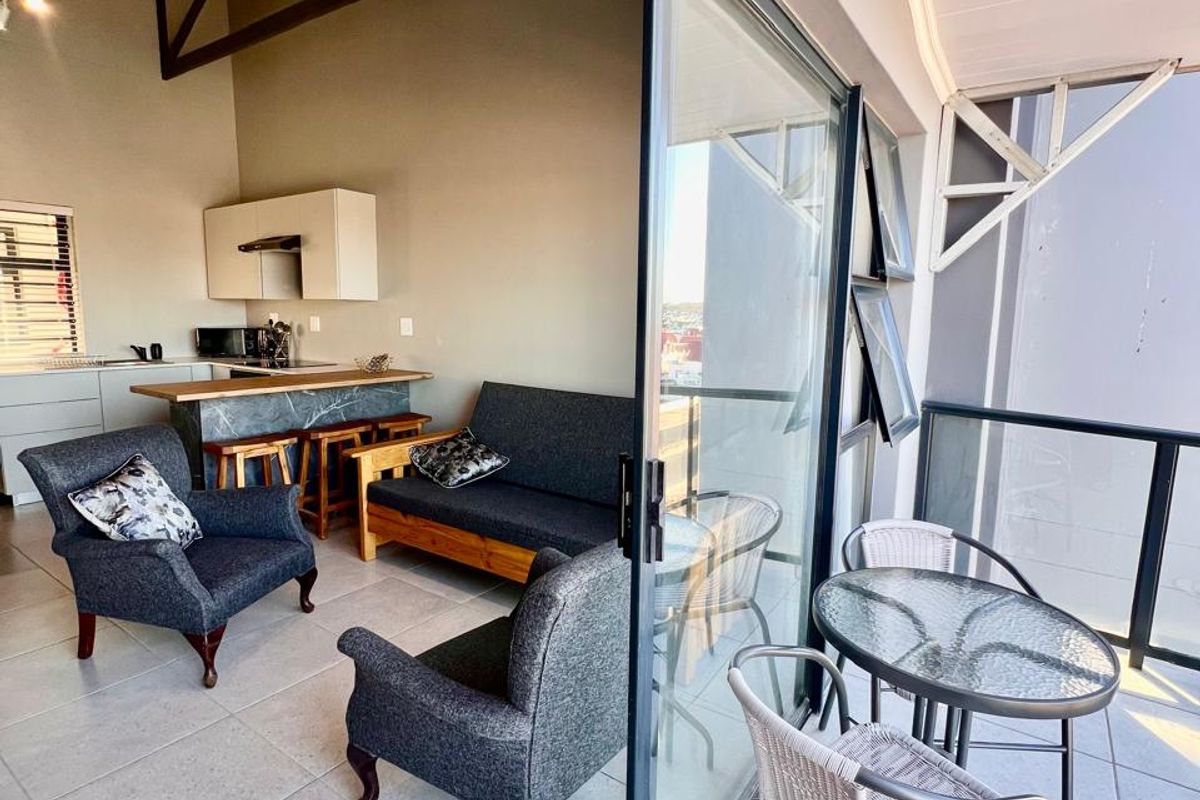 Open-plan living area featuring exposed roof trusses, a kitchen island, and seamless transition to a private balcony through large sliding glass doors.