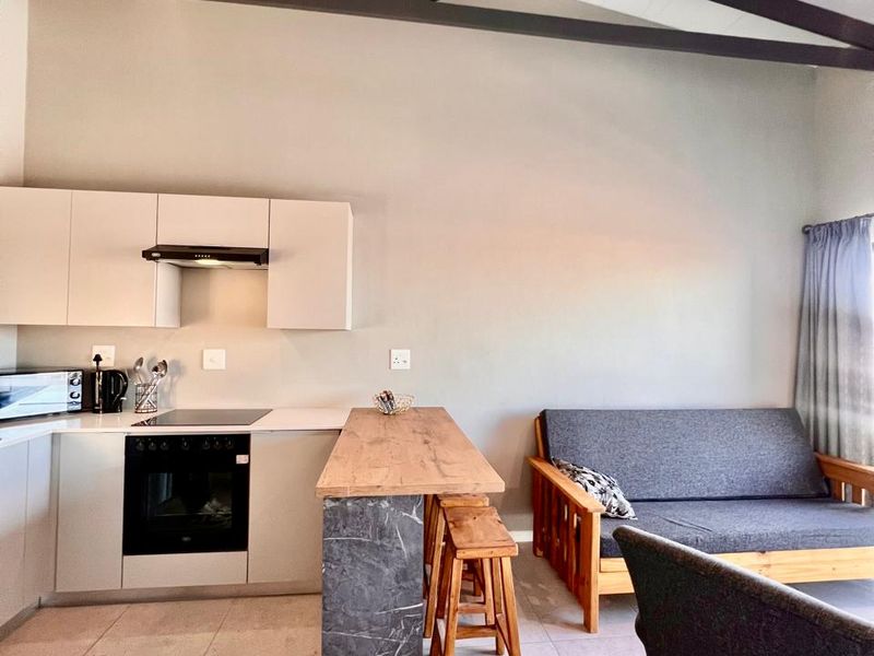 Modern open-plan living area featuring a sleek kitchen with integrated appliances, a stone-topped breakfast bar, and striking exposed roof trusses.