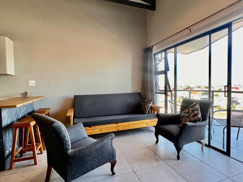 Open-plan living area featuring high ceilings with exposed beams, tiled floors, and large sliding doors leading to a balcony with natural light.