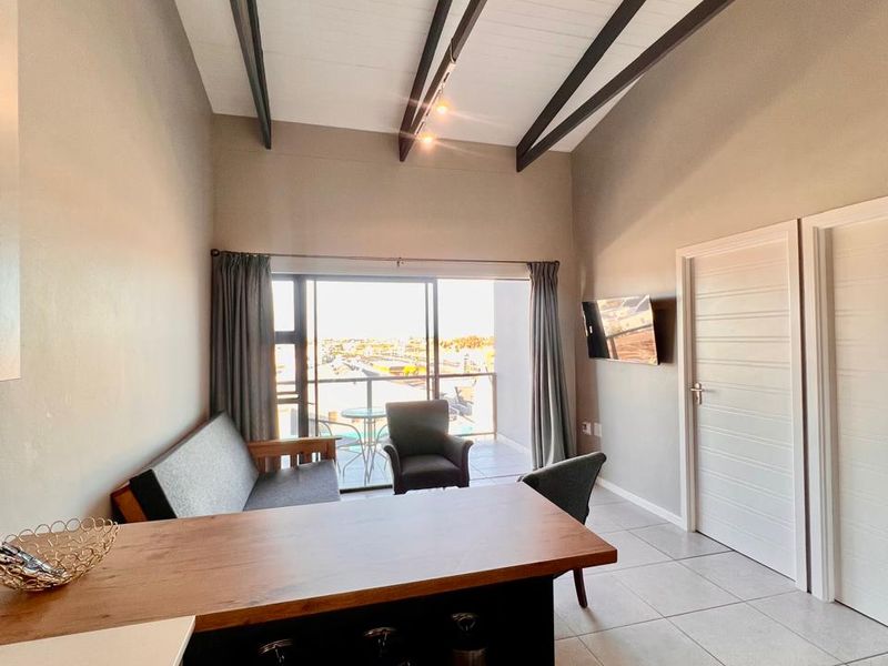 Open-plan living area featuring a vaulted ceiling with exposed beams, tiled flooring, and direct access to a private balcony through sliding glass doors.
