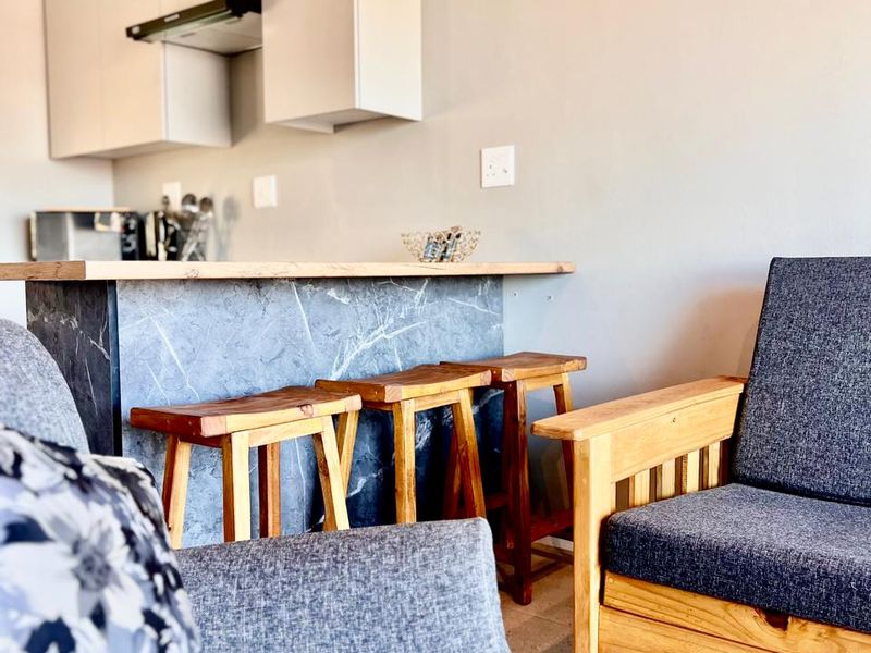 An open-plan living area featuring a modern kitchen with built-in cabinetry, an extractor fan, and a stone-look breakfast bar with tiled flooring.
